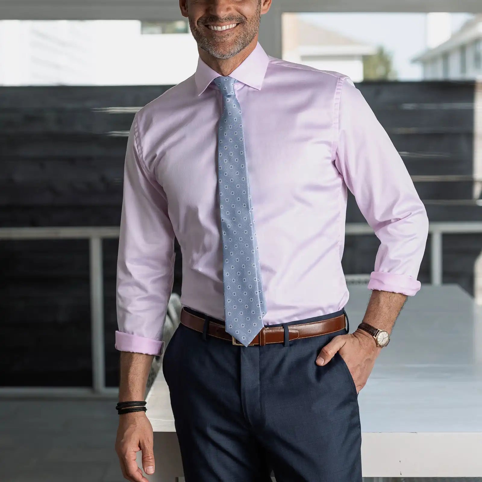 Man wearing a light pink non iron dress shirt, dark blue pants, and a light blue tie indoors.