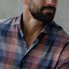 A close up of a plaid shirt in muted blues and orange tones on a man with a beard looking off to the side, with his eyes cut off just above the nose.