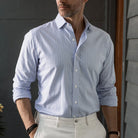 Man wearing a lavender checkered shirt and white pants against a dark background