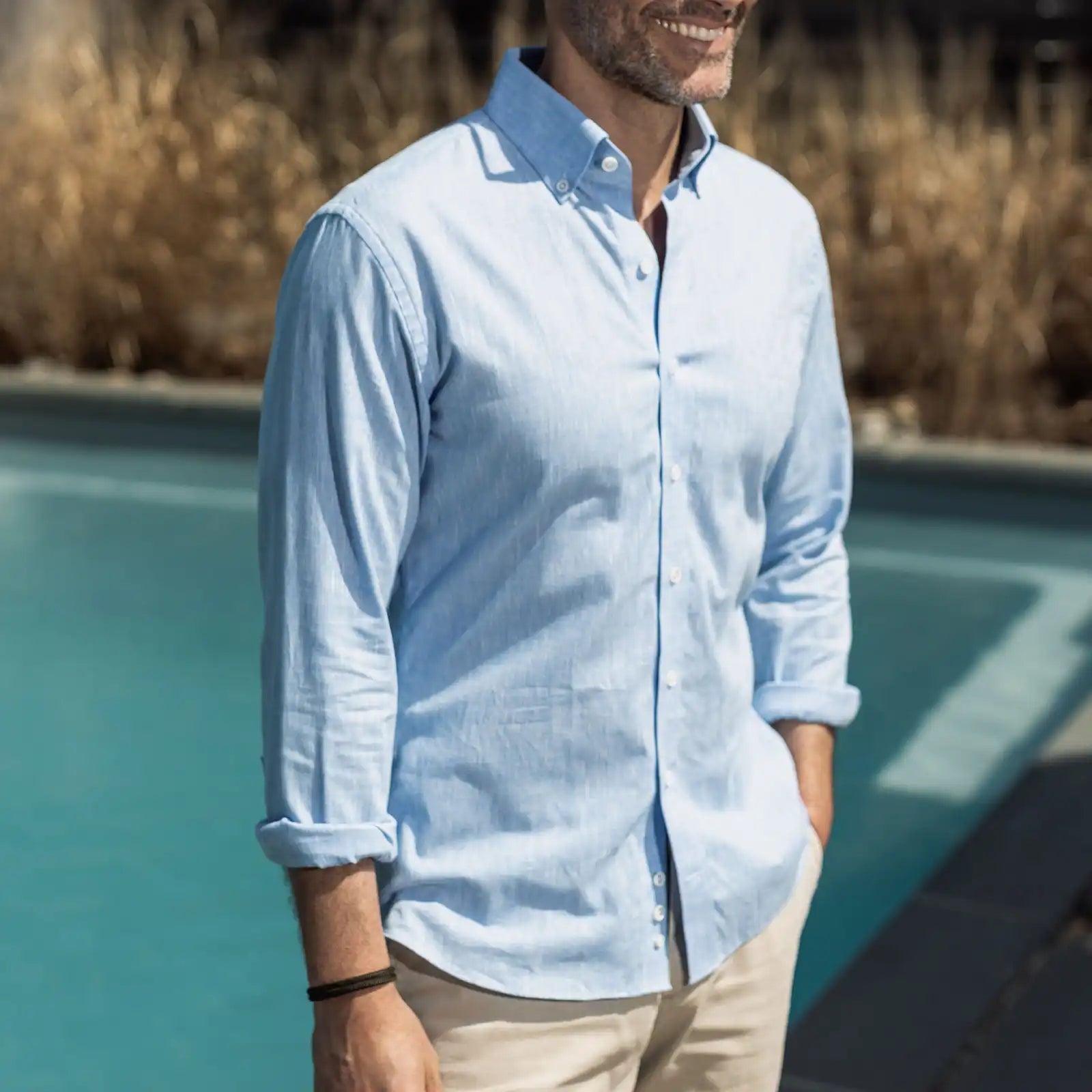 Man wearing a light blue shirt standing by a poolside with grass in the background