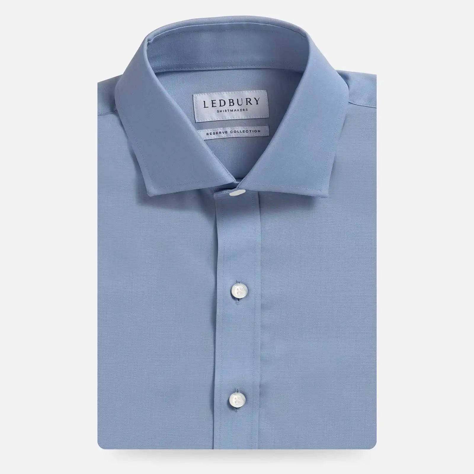 A folded light blue dress shirt with a pointed collar and white buttons, displayed on a light gray background. The inner neck label shows the brand 'LEDBURY'.