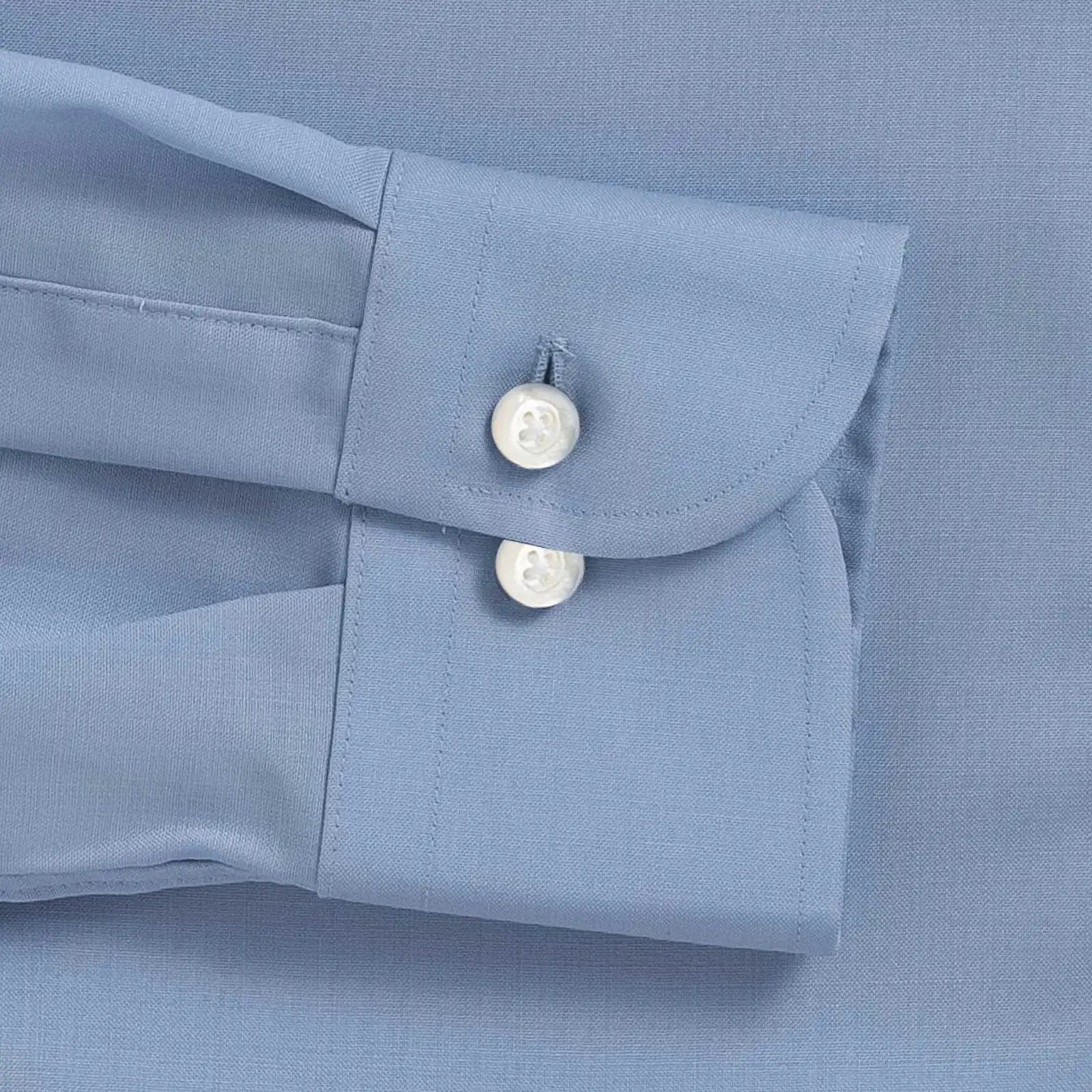 Close-up of a light blue dress shirt cuff with two white mother of pearl buttons on a matching blue fabric background.