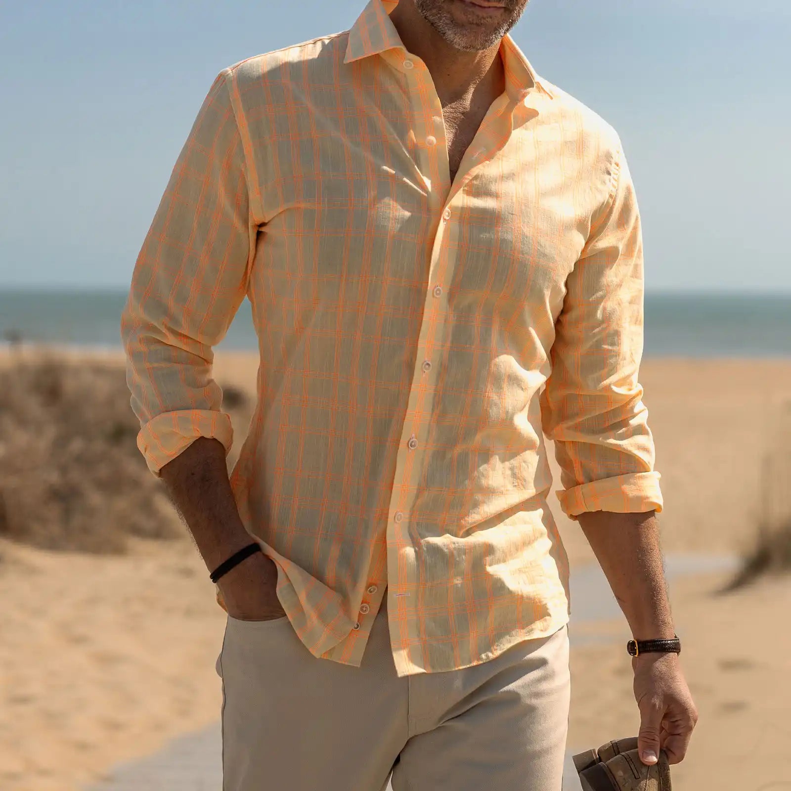 Man wearing a bright yellow and orange checkered shirt on a beach