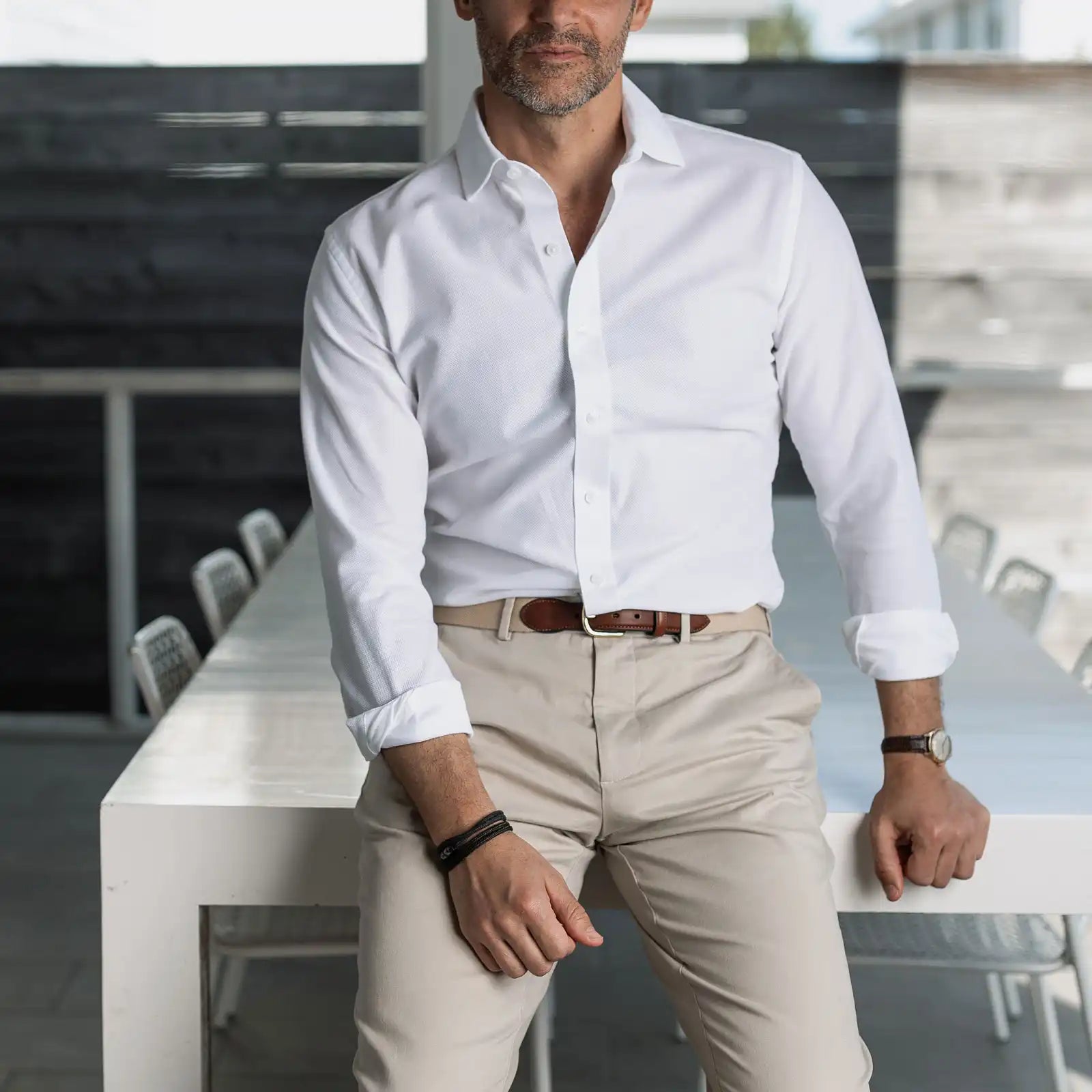 Man wearing a breathable white shirt and beige pants leaning against a white table.