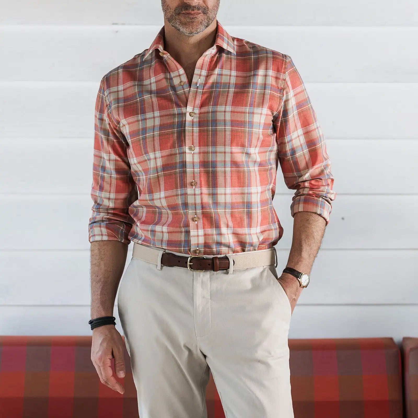 Man wearing a red plaid shirt and white pants against a white wall.