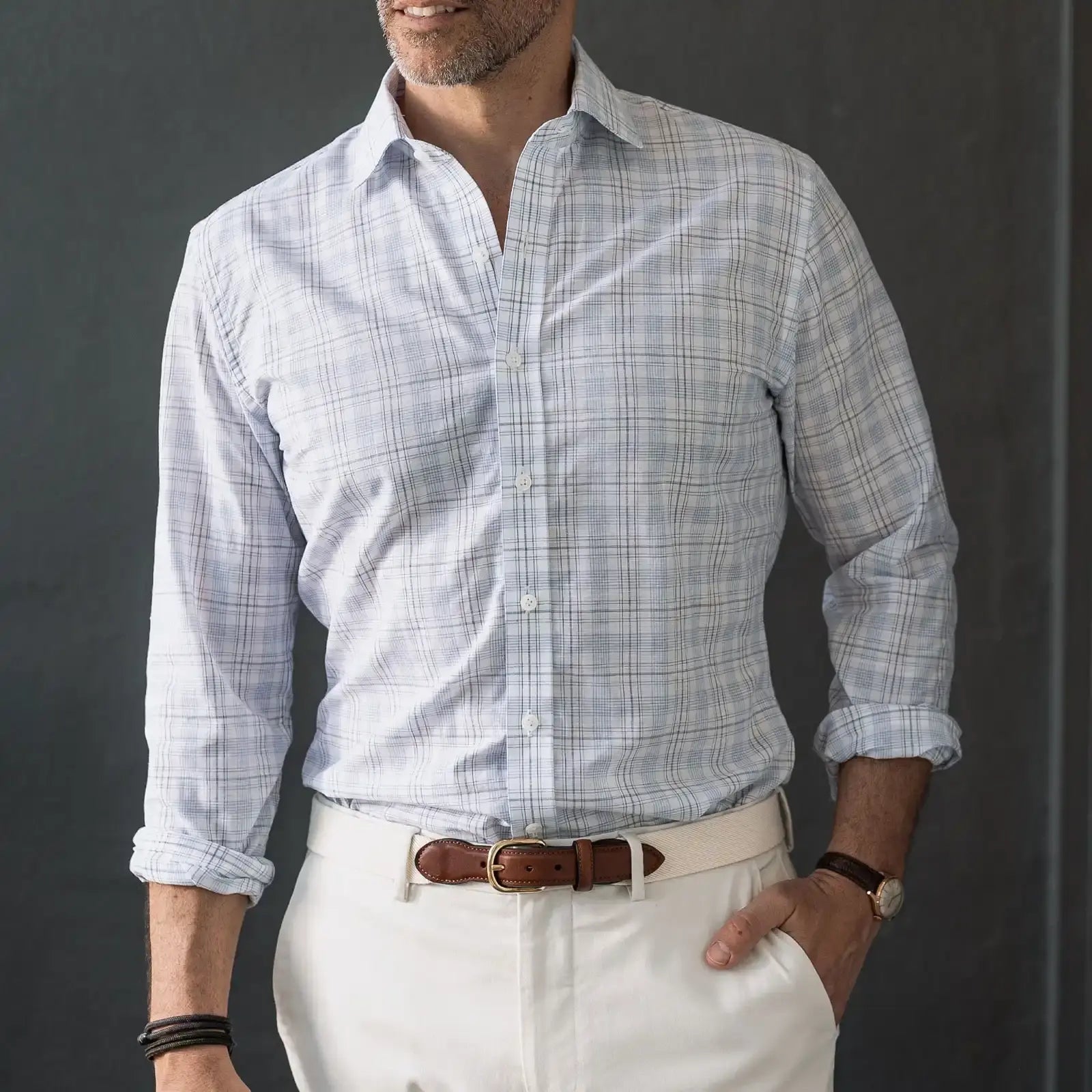 Man wearing a light blue checkered shirt and white pants against a dark background