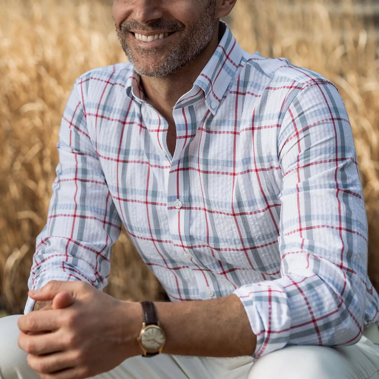 Man wearing the Ledbury Red Pepper Bartlett Plaid shirt in a field — pepper red, white, and blue cotton seersucker
