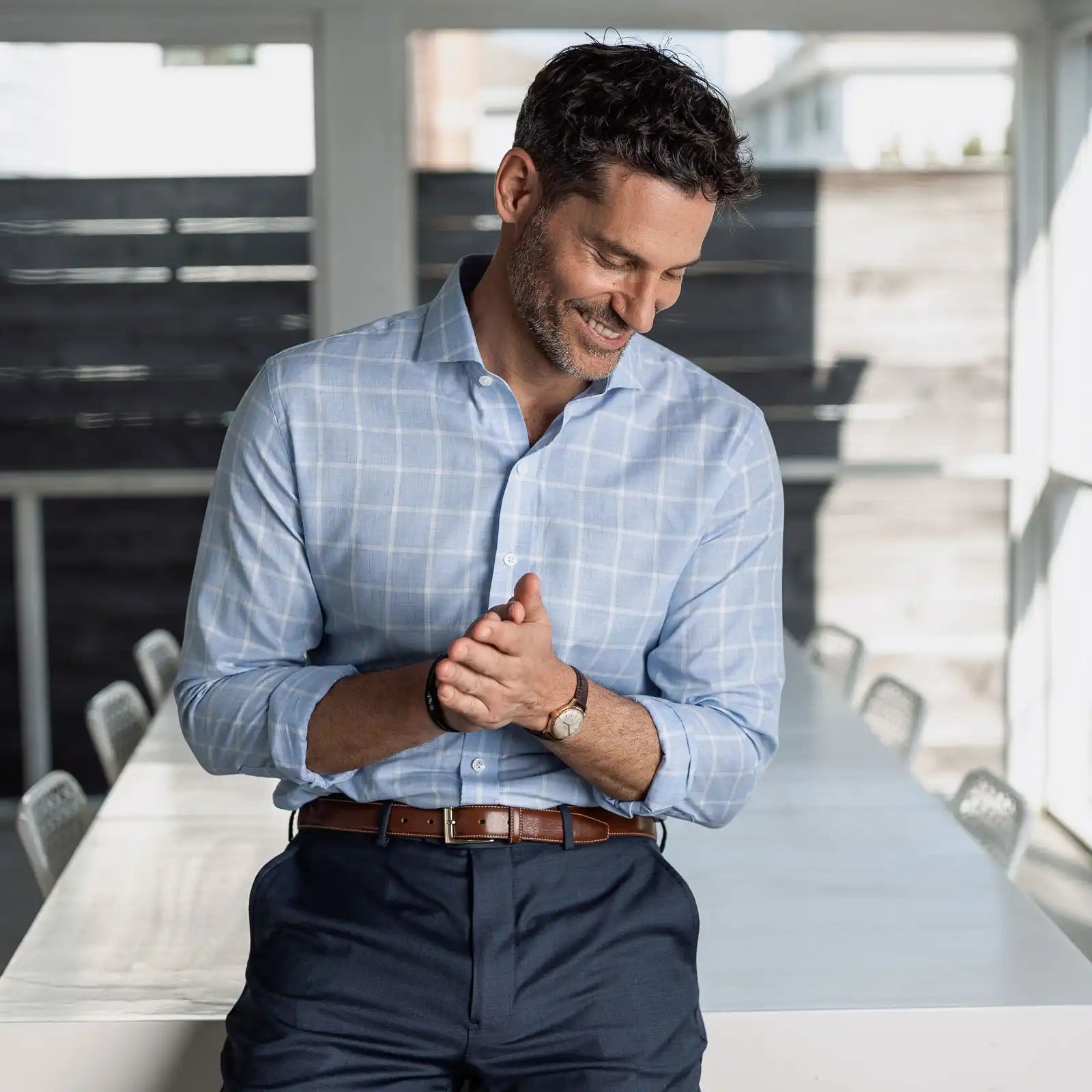Man wearing a light blue checkered shirt and dark pants in a modern room.