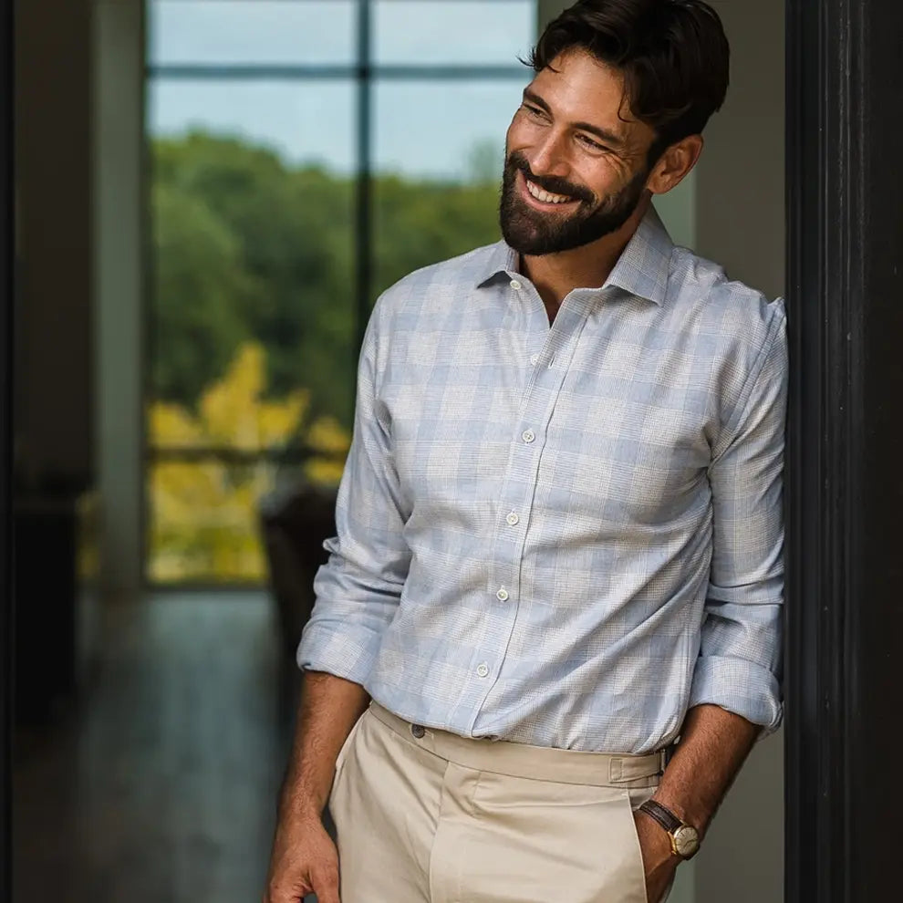Man wearing a light blue and light grey business casual flannel shirt, standing in a doorway. 