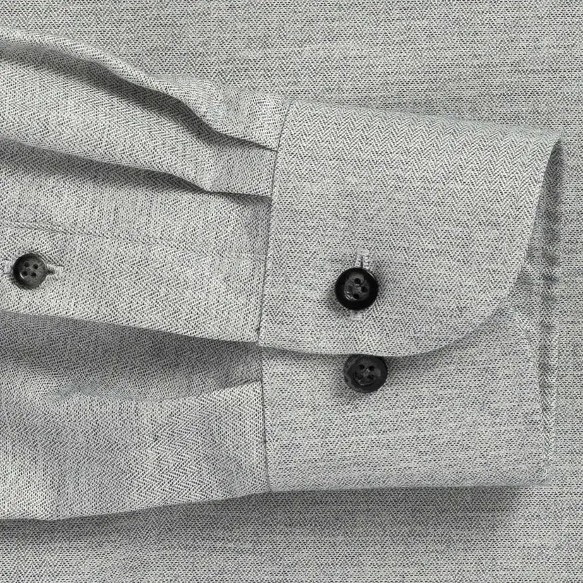 Close up of the sleeve of a grey small scale herringbone dress shirt with black buttons