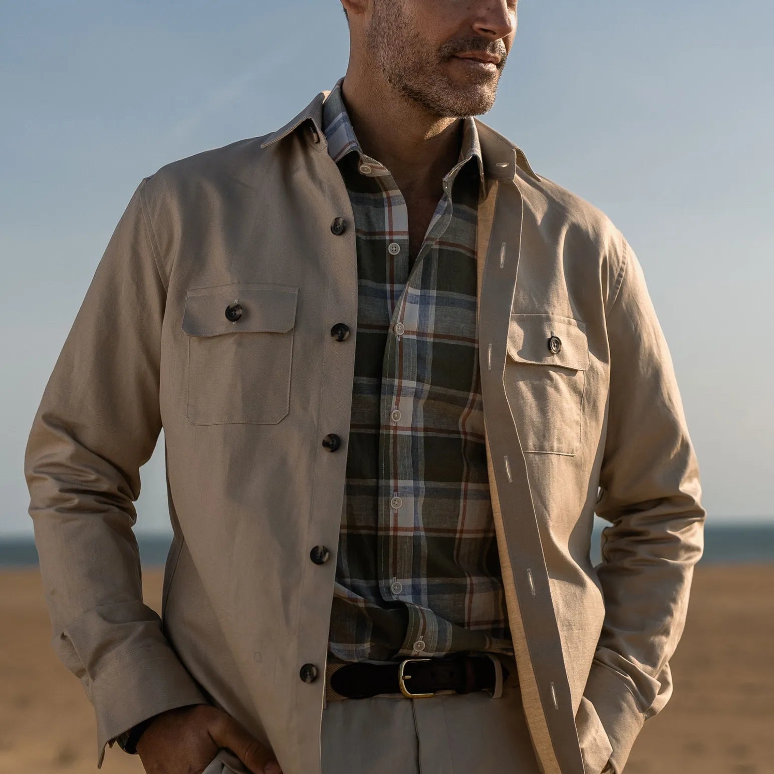 Man wearing a light tan shirt jacket over a plaid shirt with a blurred background