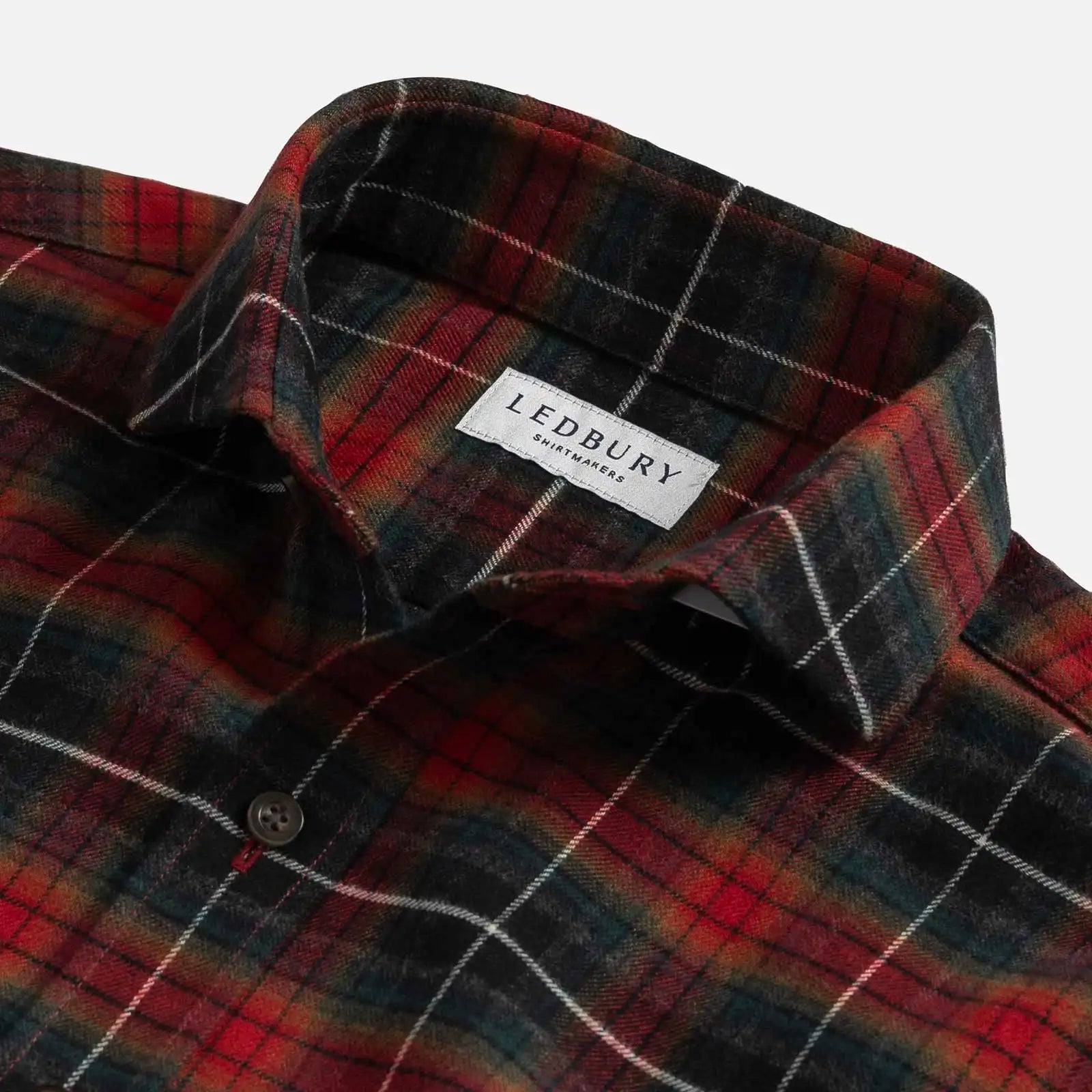 Close-up of a Ledbury plaid shirt in red, black, and green with white windowpane lines, showing the collar and button.