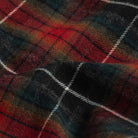 A close-up of a plaid fabric with a tartan pattern in red, black, and green, accented by thin white diagonal stripes.