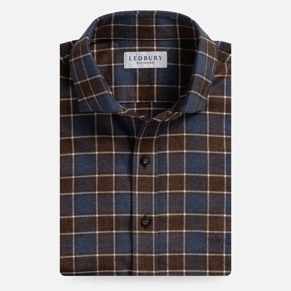 A folded men's button-up shirt by Ledbury, featuring a classic plaid pattern in dark brown, slate blue, and thin cream stripes, set against a plain light gray background.