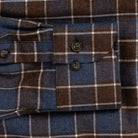 Close-up of a plaid buttoned cuff on a blue and brown flannel-style shirt, showing the fabric texture and dark buttons.