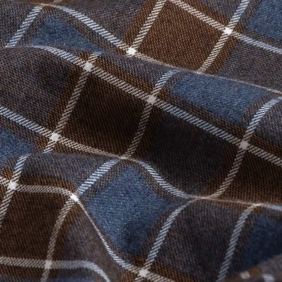 A close-up of a plaid fabric with a blue and brown checkered pattern, accented by thin white diagonal stripes.