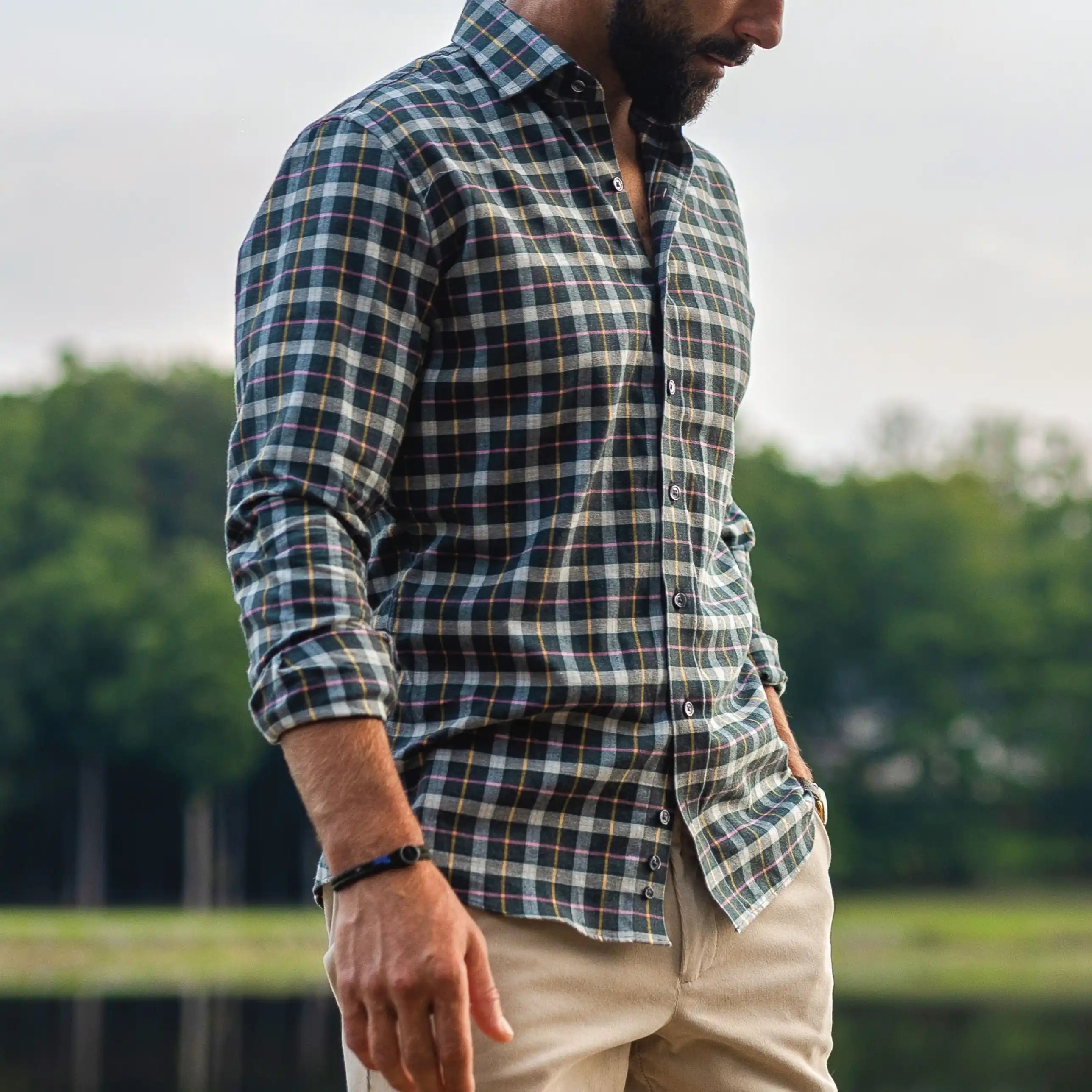 Man wearing a dark green, cream, and pink flannel in an outdoor setting