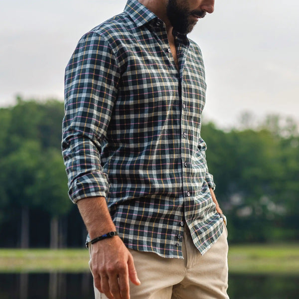 Man wearing a dark green, cream, and pink flannel in an outdoor setting