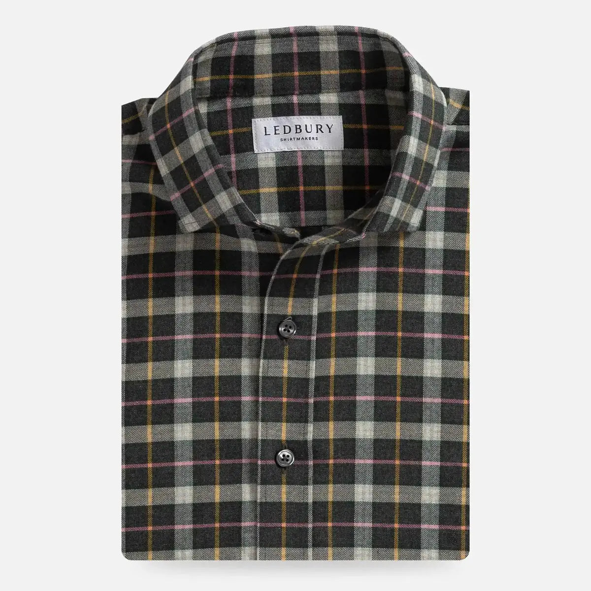 A folded long-sleeve plaid shirt by Ledbury, featuring a dark gray and black base with beige, yellow, and pink intersecting stripes, shown on a light gray background.