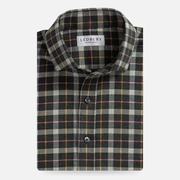 A folded long-sleeve plaid shirt by Ledbury, featuring a dark gray and black base with beige, yellow, and pink intersecting stripes, shown on a light gray background.