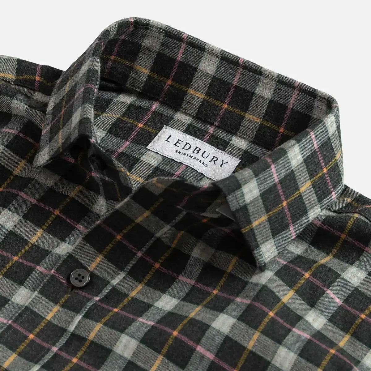 Close-up of a plaid button-down shirt collar with a visible LEDBURY label. The fabric has a dark charcoal base with intersecting gray, white, yellow, and pink plaid lines.