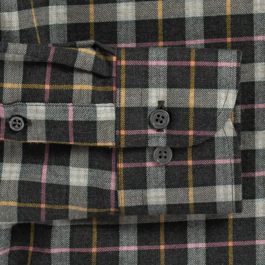 Close-up of a plaid button-up shirt fabric with a dark charcoal base, white and gray checks, and thin yellow and pink stripes. The shirt features a chest pocket with two dark buttons and a matching buttoned cuff.