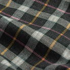 A close-up of a plaid fabric with a black, gray, and white tartan pattern accented by thin yellow and pink stripes.