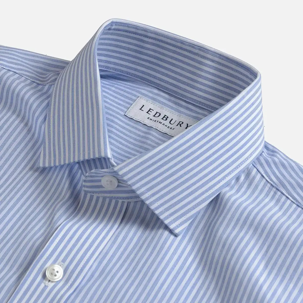 Close-up of a Ledbury men's dress shirt in a light blue and white stripe pattern, showing the collar, button, and brand label.