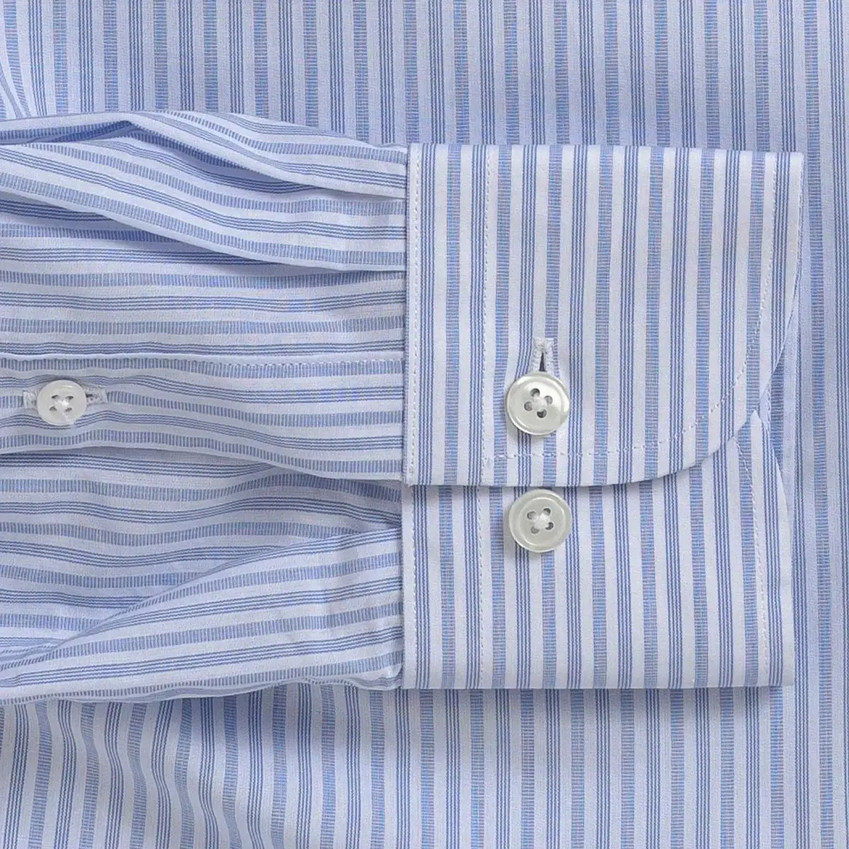 Close-up of a light blue and white striped dress shirt cuff with two white buttons, laid flat against the matching striped fabric.