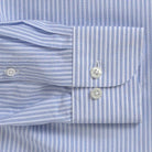 Close-up of a light blue and white striped dress shirt cuff with two white buttons, laid flat against the matching striped fabric.