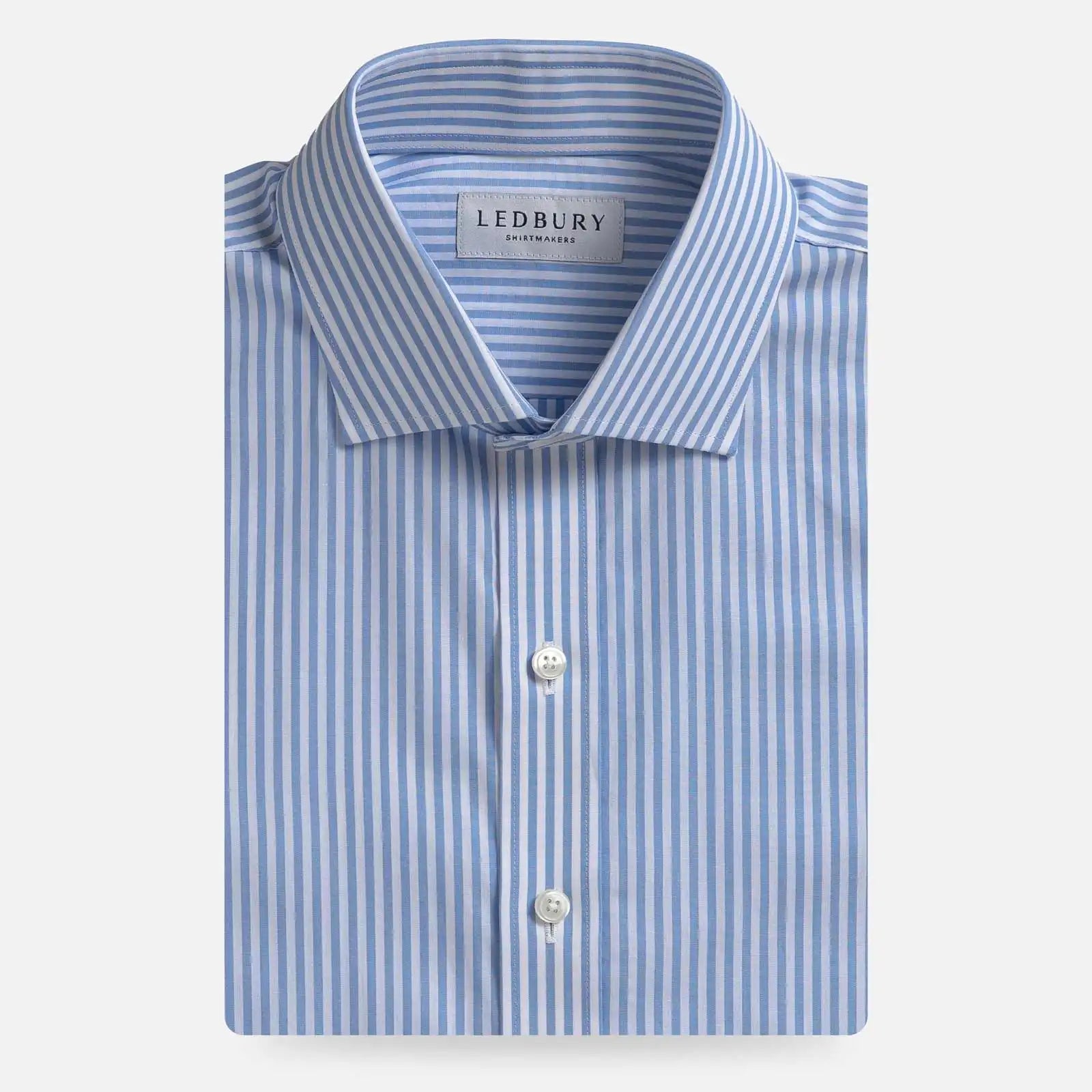 A folded men's dress shirt by Ledbury, featuring light blue and white vertical stripes, a classic collar, and white buttons, set against a clean off-white background.