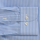 Close-up of a light blue and white striped dress shirt showing the buttoned cuff and front placket.