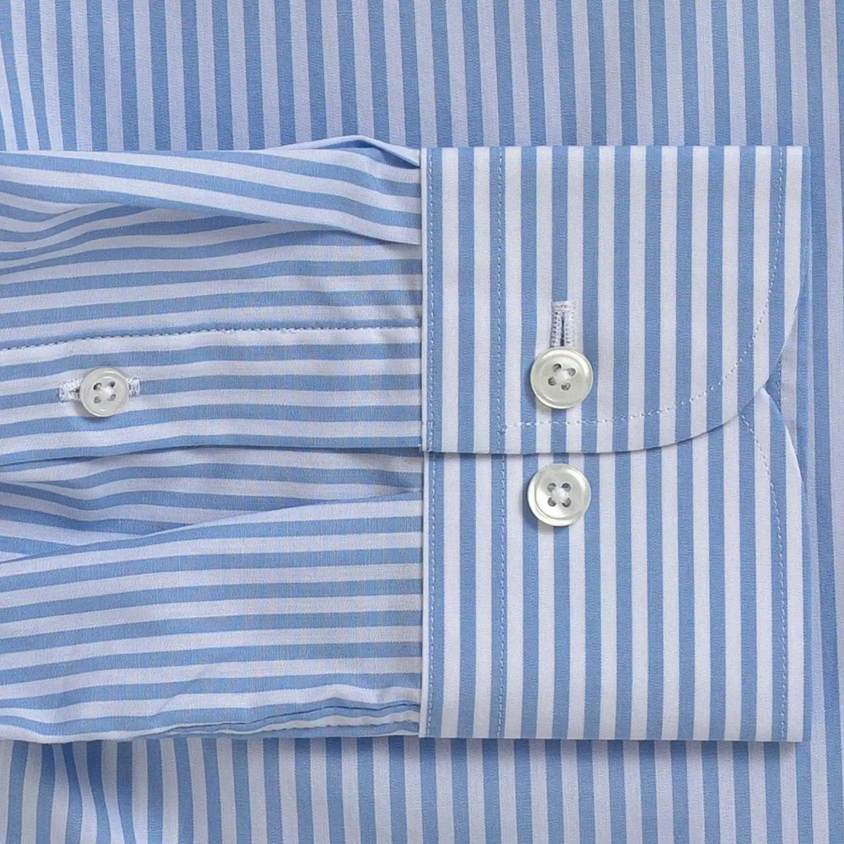 Close-up of a light blue and white striped dress shirt showing the buttoned cuff and front placket.