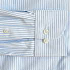 Close-up of a light blue and white striped dress shirt cuff with two white buttons, showing the fabric texture and pattern details.