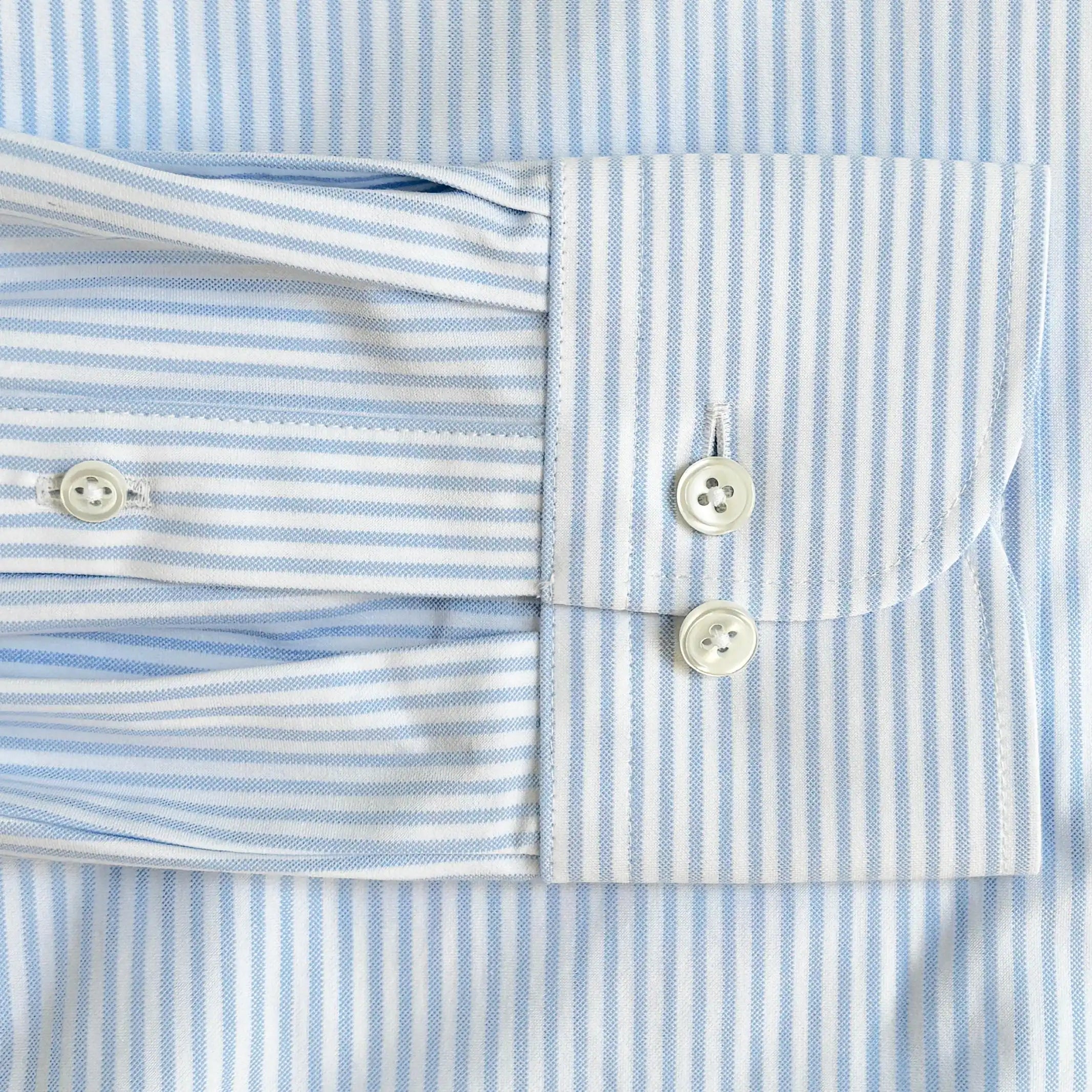Close-up of a light blue and white striped dress shirt cuff with two white buttons, showing the fabric texture and pattern details.