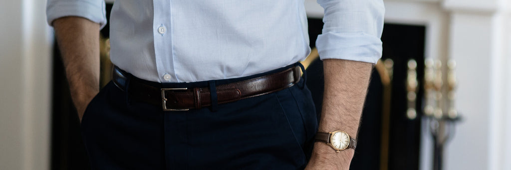 Closeup of a men's leather belt worn by a male model standing in front of a fireplace.