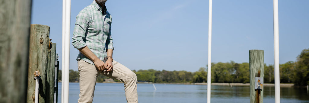 Image of a model standing on a dock wearing a button down shirt and tan chinos