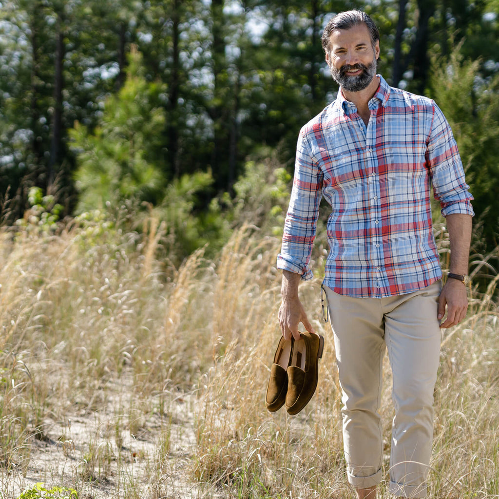 Image of a model wearing a plaid button down shirt walking in a field of tall grass