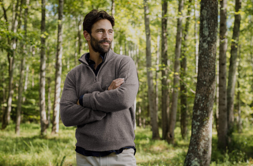 Man standing in the woods wearing a half zip tan sweater
