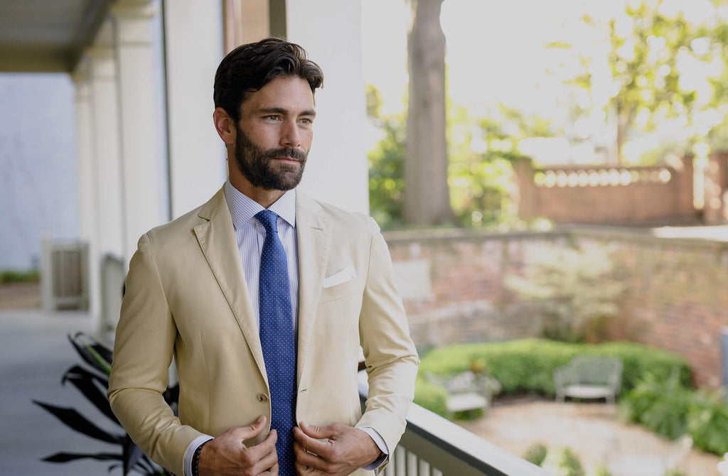 Man outdoors on back deck wearing a striped dress shirt, a navy tie, and a tan sport coat.