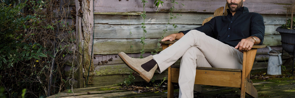 Man sitting in wooden outdoor chair wearing tan Richmond chino pants and brown boots.