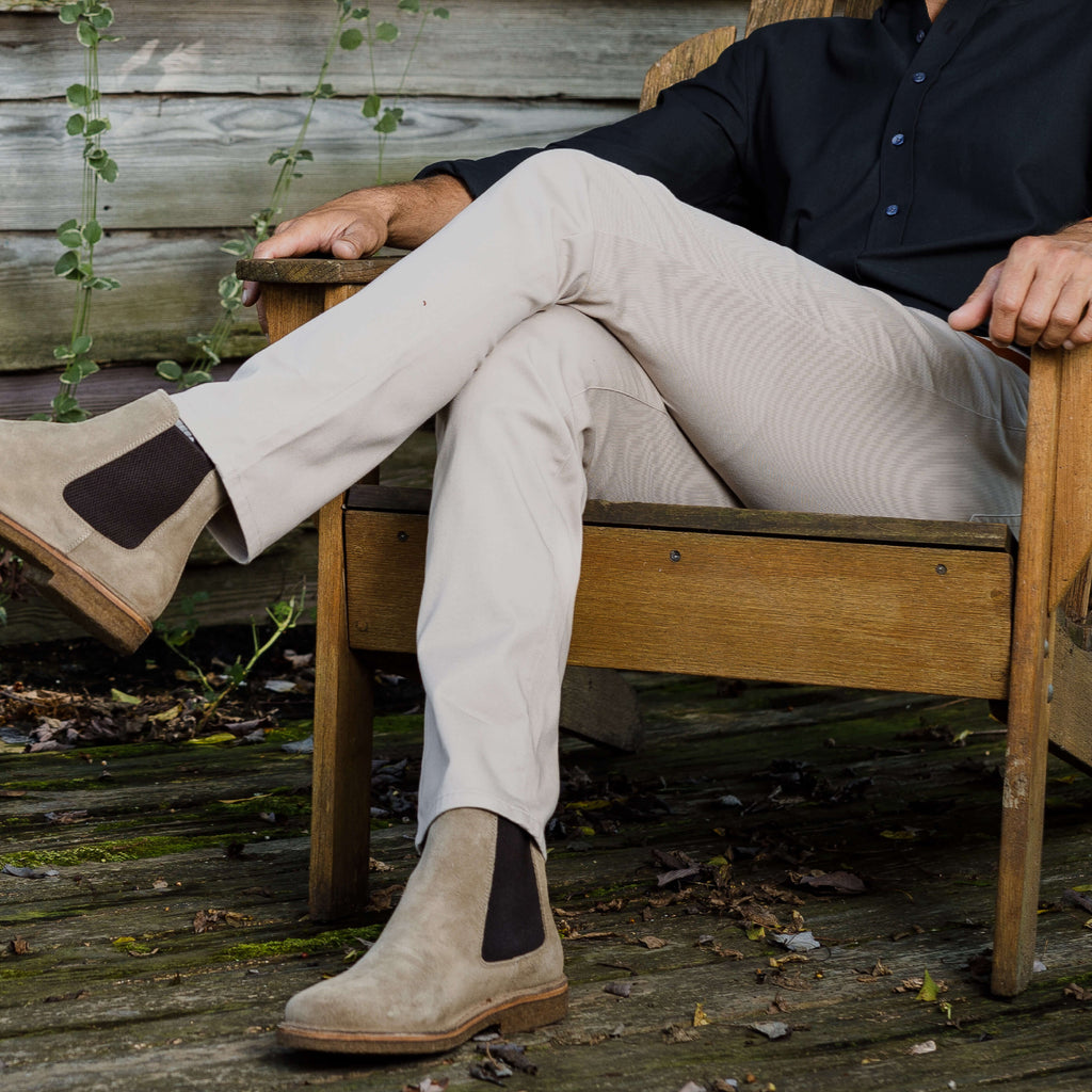 Man sitting in wooden outdoor chair wearing tan Richmond chino pants and brown boots.