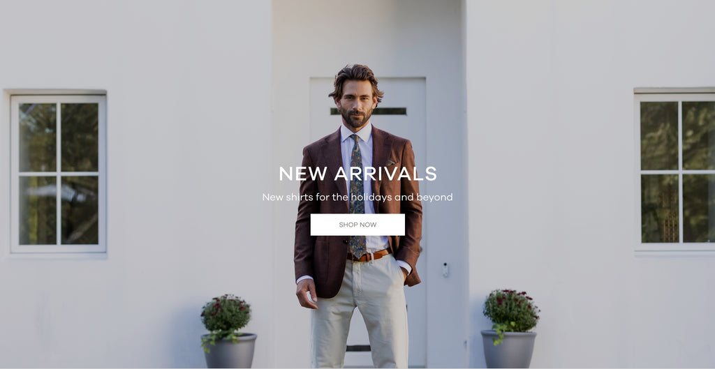 A man wearing a white dress shirt and a brown sports coat in front of a white house. The image says "New Arrivals. New Shirts for the holidays and beyond. Shop Now."