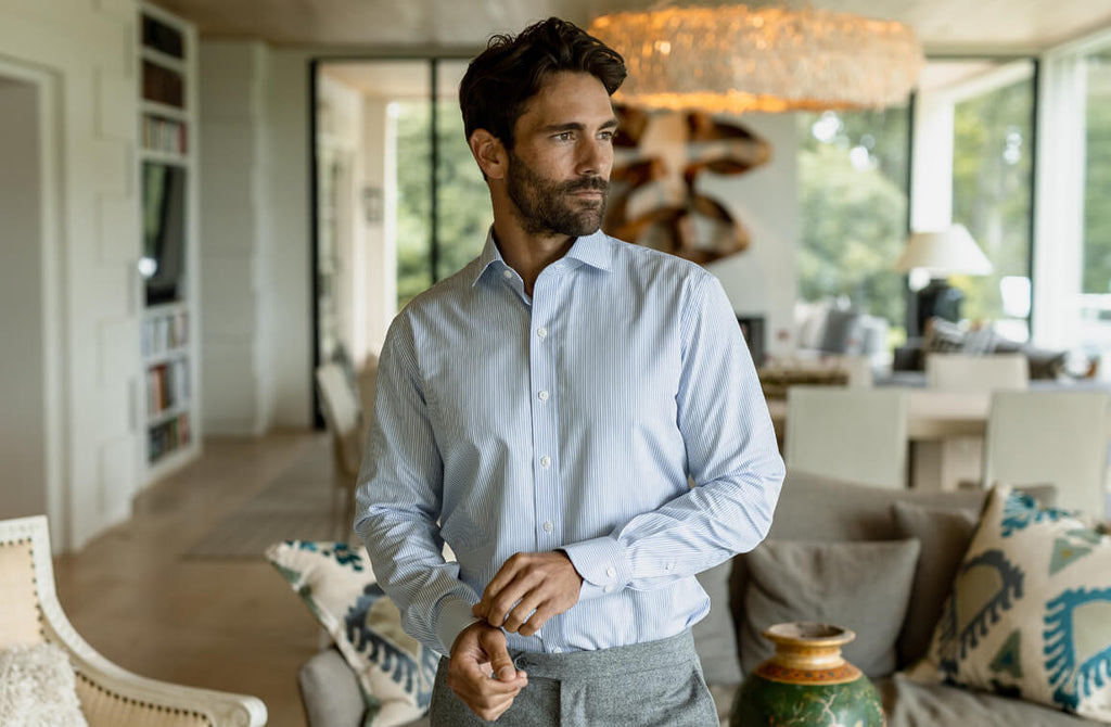 Male model wearing a men's light blue dress shirt standing inside a living room