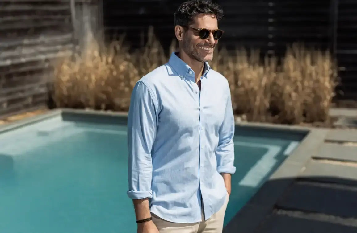 Man wearing a long sleeve blue button down shirt standing in front of a swimming pool 