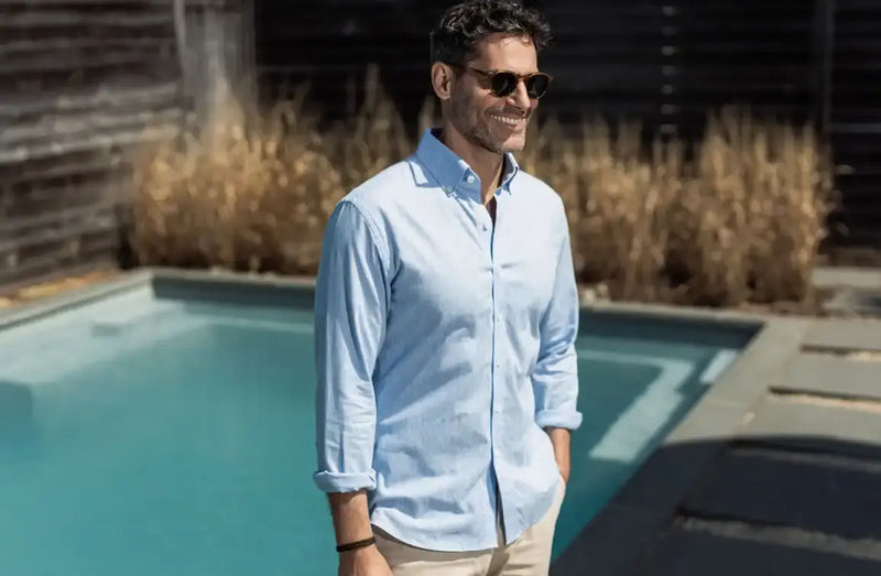 Man wearing a long sleeve blue button down shirt standing in front of a swimming pool 