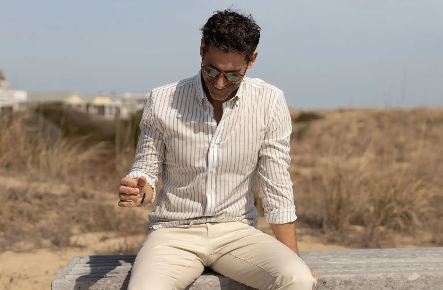 Man sitting on a bench at the beach wearing a striped linen cotton shirt