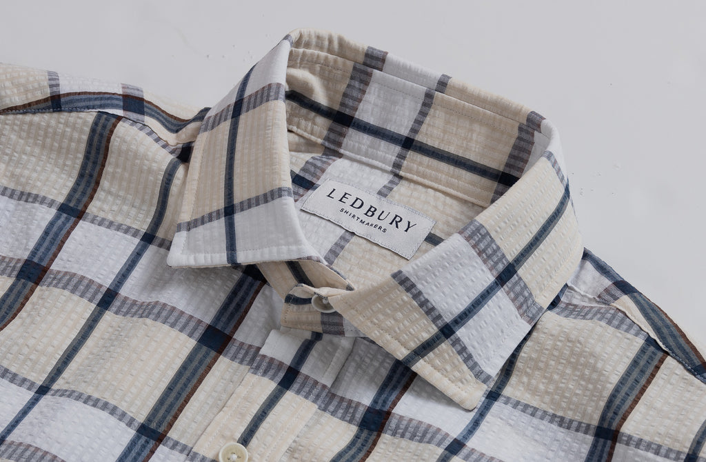 Closeup of the collar of a men's tan, white, and navy plaid seersucker button up shirt
