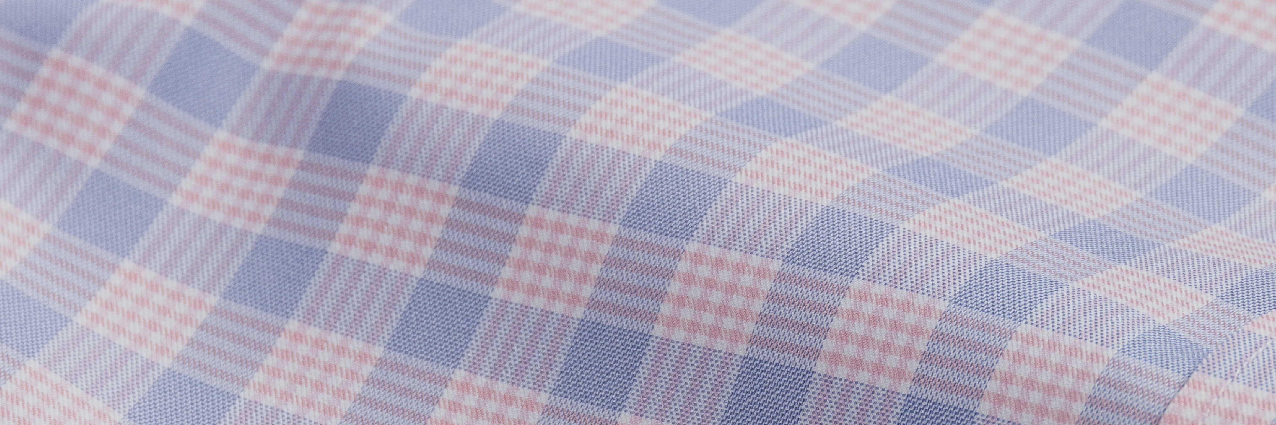 Closeup of the fabric of a men's breathable performance fabric button down shirt in a pink and blue plaid pattern. 