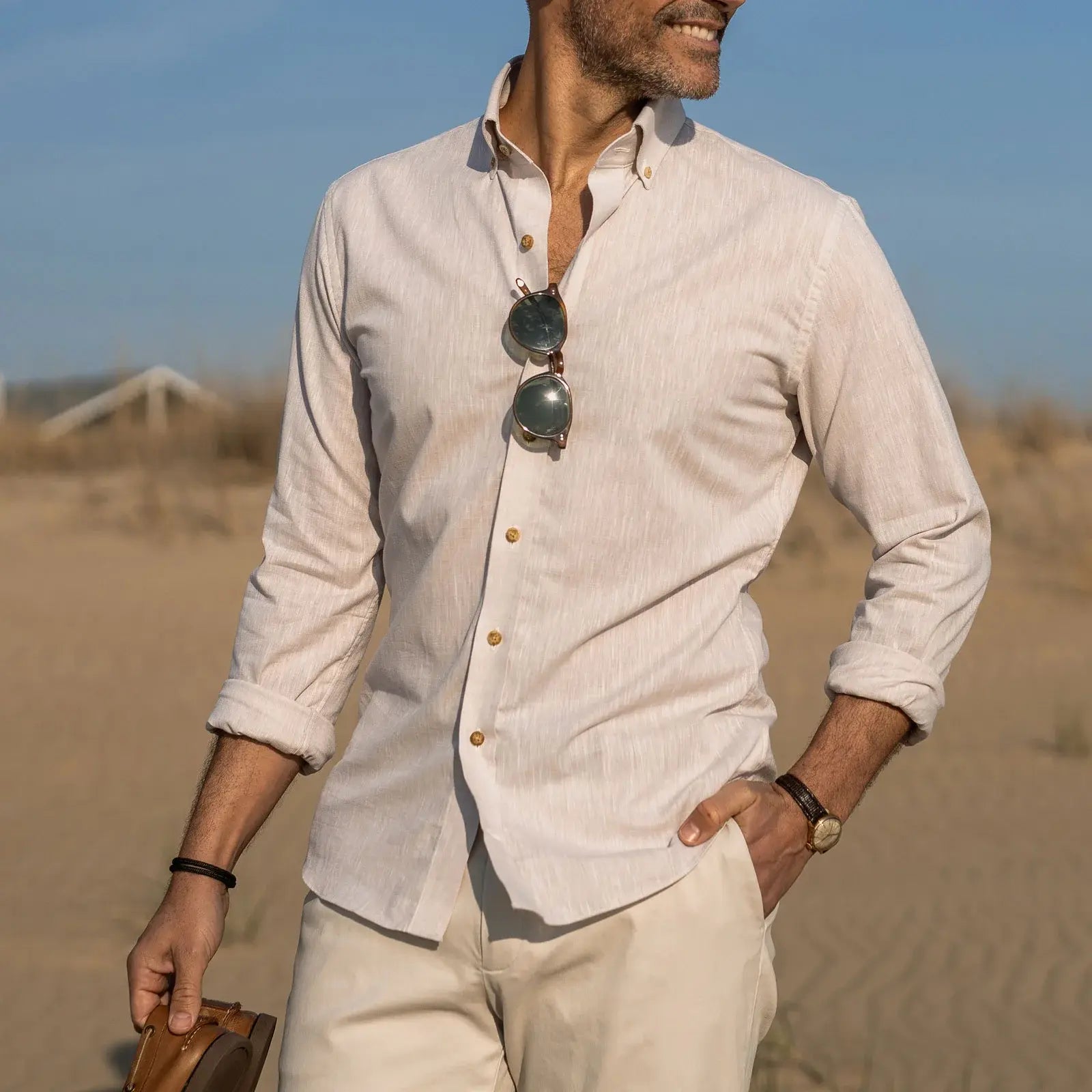 Man wearing a light-colored Ledbury button down shirt with rolled-up sleeves in a beach setting
